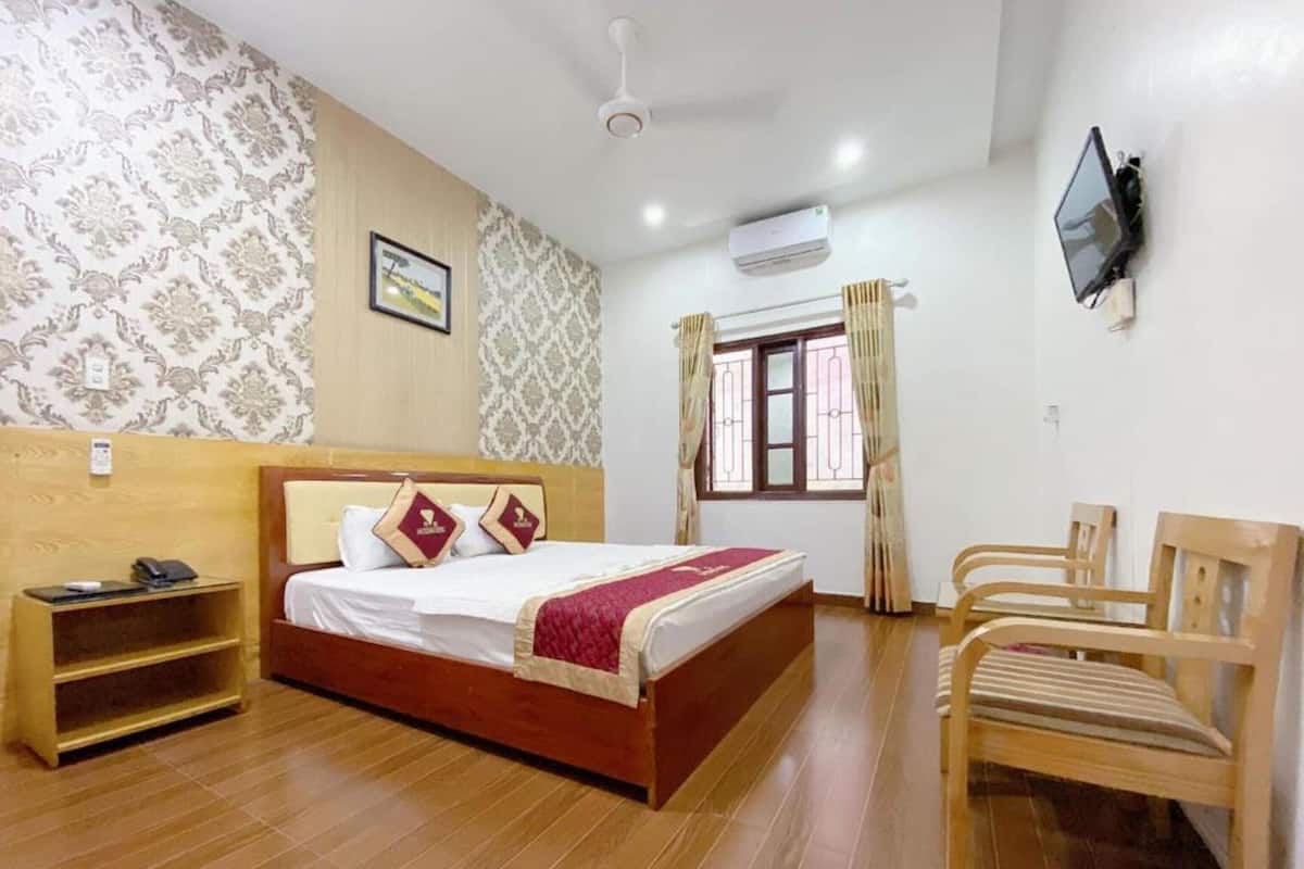 A hotel room with a wooden bed, a desk with a phone, a TV mounted on the wall, and a window with curtains.
