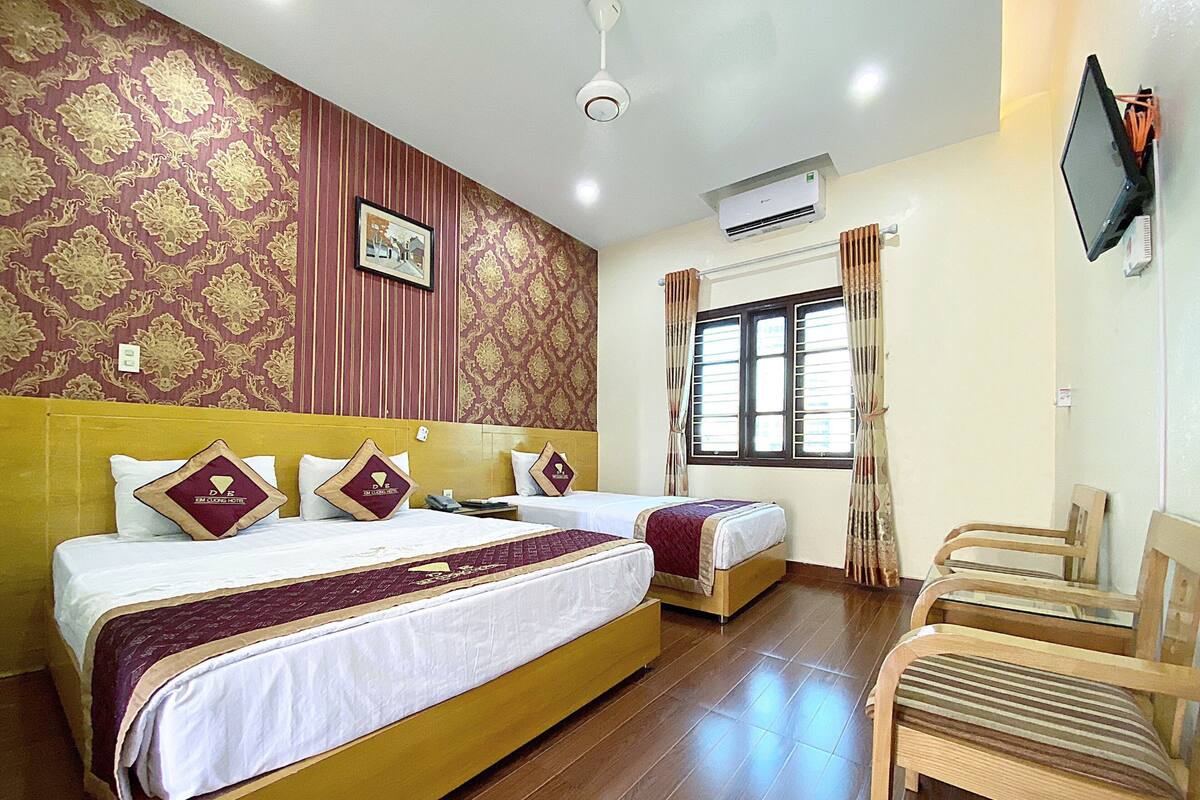 A hotel room with two beds, a TV, and a window with curtains.