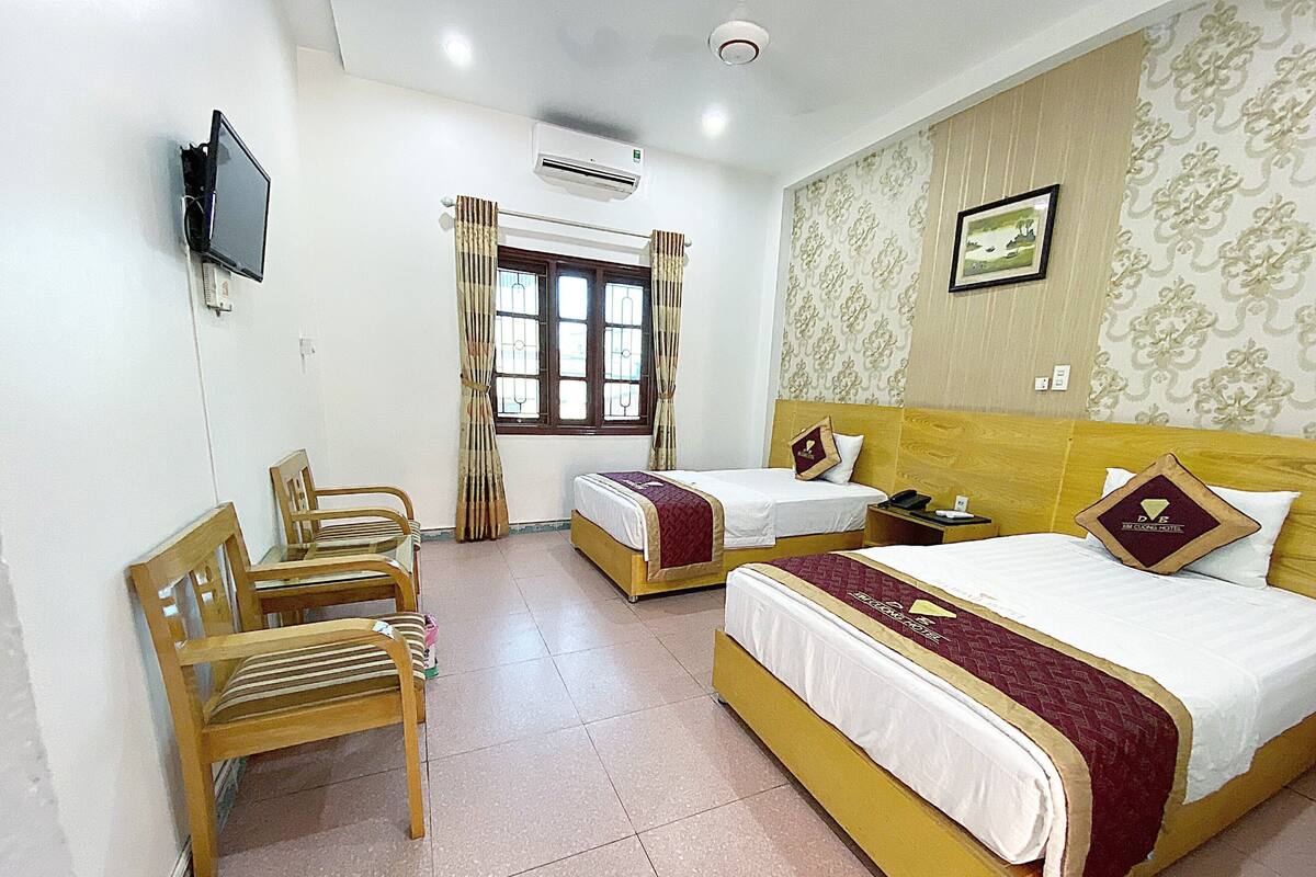 A hotel room with two beds, a TV, a chair, a window with curtains, and a patterned wall.