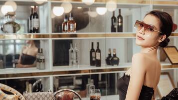 A woman in a black dress standing at a bar with a display of liquor bottles behind her.