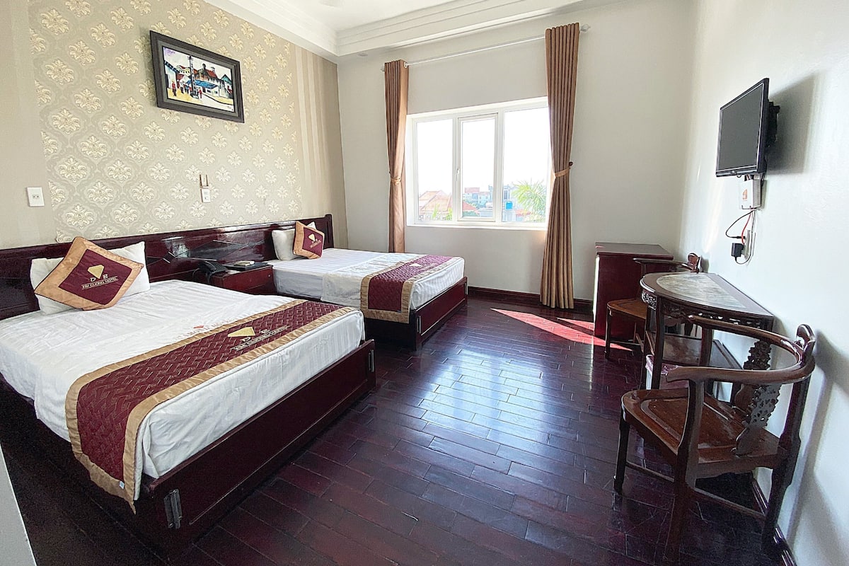 A hotel room with two beds, a desk, a chair, a TV, and a window with curtains.