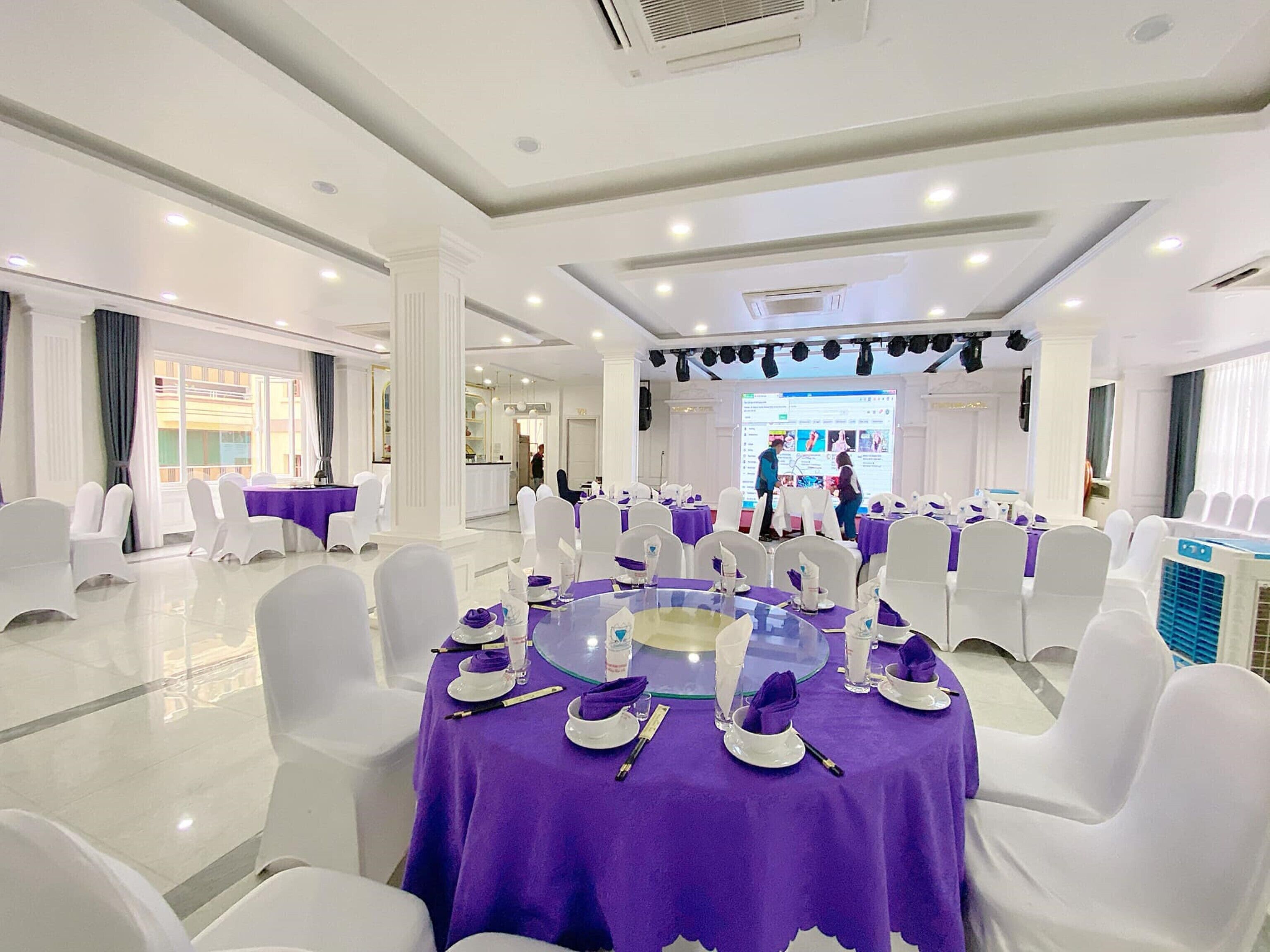 Un salón de conferencias con mesas redondas, sillas blancas y manteles morados.