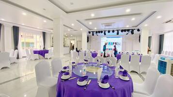Un salón de conferencias con mesas redondas, sillas blancas y manteles morados.