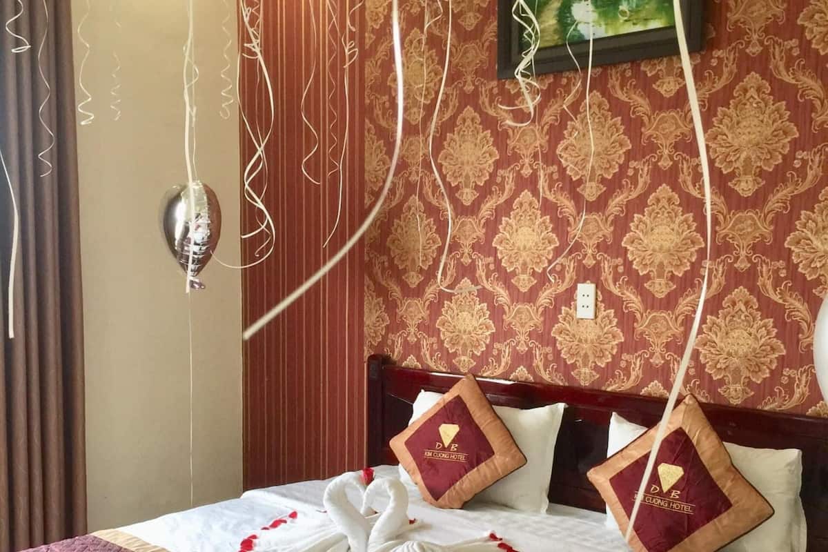 A hotel room with a neatly made bed, a painting on the wall, and a decorative pillow with a logo.