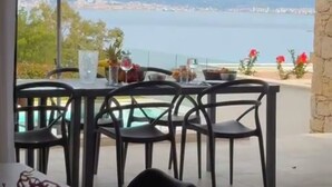 Een terras met een tafel en stoelen, een paarse parasol en uitzicht op zee en bergen.