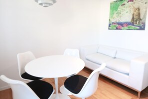 Een moderne kamer met een witte bank, een klein rond tafeltje en twee witte stoelen met zwarte kussens.