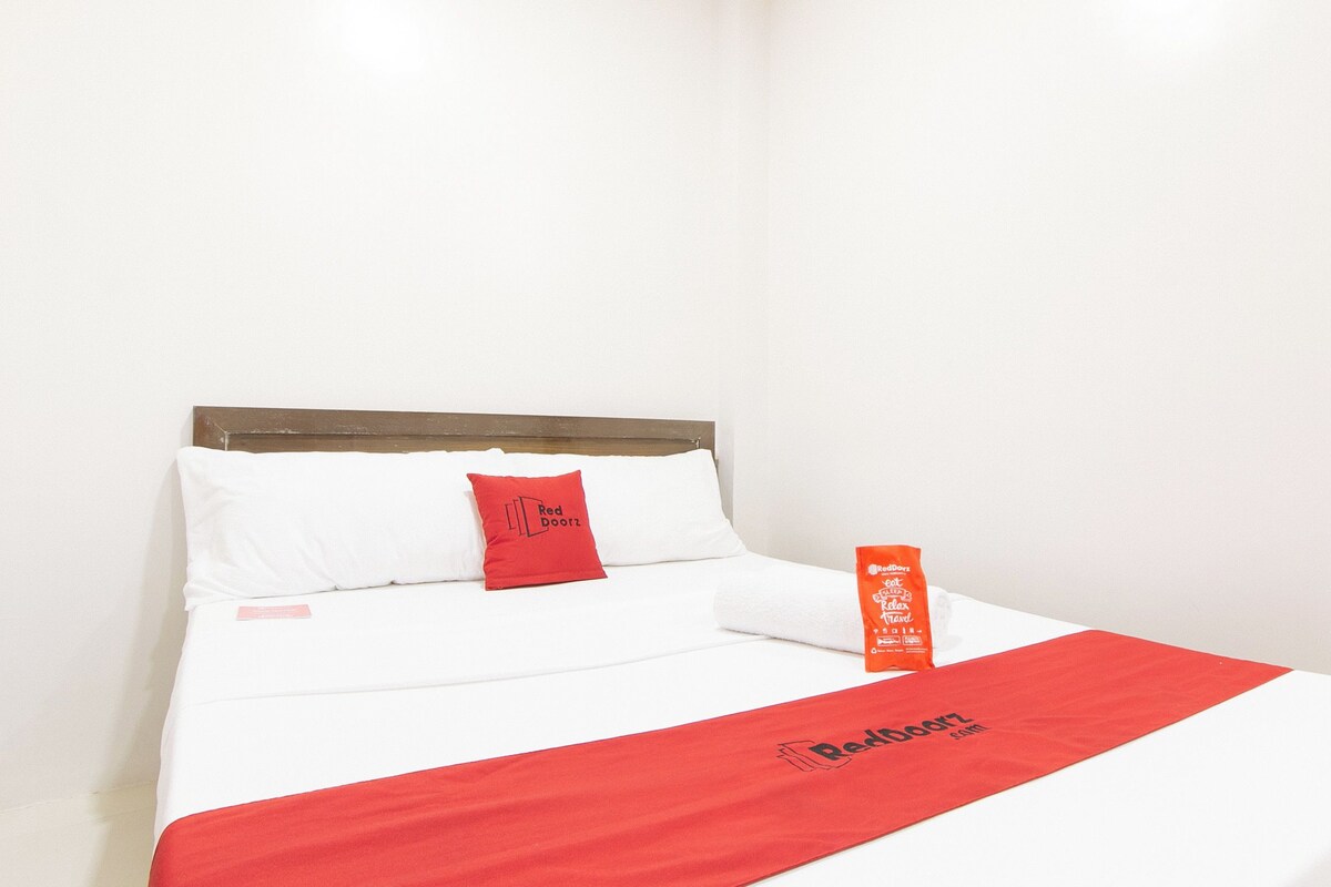 A hotel room with a bed, a red pillow, a red blanket, and a bottle of Red Doorz bath salts.