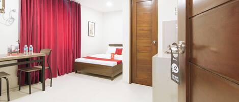 A hotel room with a wooden bed, a desk with chairs, a red curtain, and a door with a do not disturb sign.