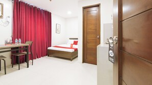 Habitación de hotel con una cama de madera, un escritorio con sillas, una cortina roja y una puerta con el letrero de 'No molestar'.