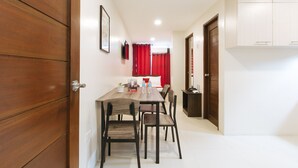 A hotel room with a wooden door, a dining table with chairs, a small table with a telephone and a plant, and a bed with red curtains. - Reddoorz Near Fernwoods Garden Quezon City (Quezon City)
