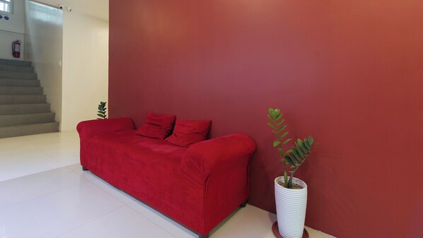 Un sofá rojo frente a una pared roja, con una planta en maceta a un lado.