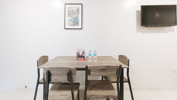 A dining area with a wooden table and four chairs, two water bottles, and a framed picture on the wall. - Reddoorz Near Fernwoods Garden Quezon City (Quezon City)