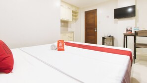 Habitación de hotel con cama, puerta de madera, televisor montado en la pared y una mesita con una botella y una caja.