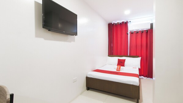 Una habitación de hotel con una cama, un televisor en la pared y cortinas rojas.