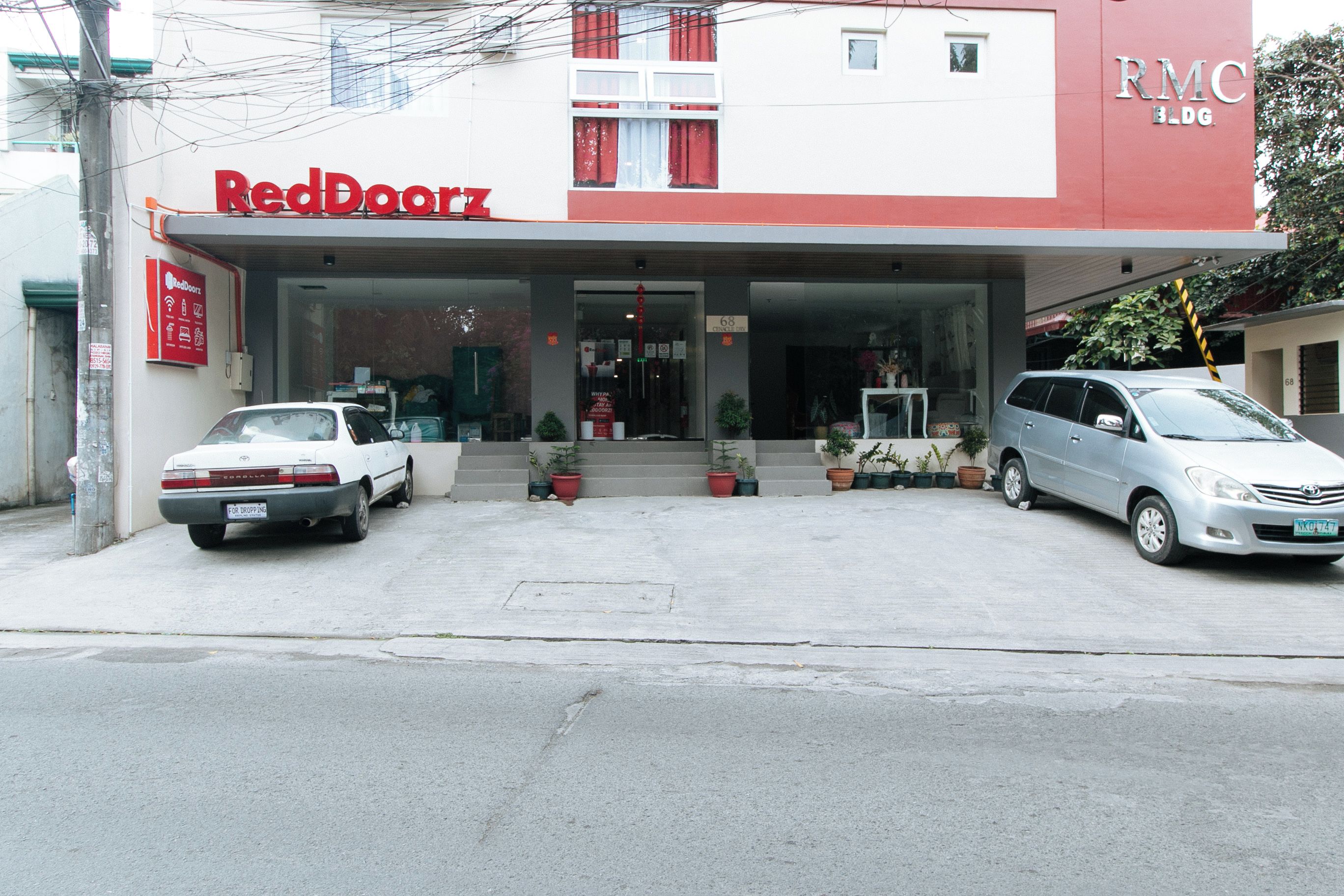 Ein RedDoorz-Gebäude mit zwei geparkten Autos davor.