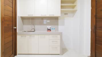 A small kitchenette with a sink, cabinets, and a hanging clothes rack.