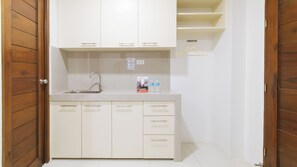 A small kitchenette with a sink, cabinets, and a hanging clothes rack. - Reddoorz Near Fernwoods Garden Quezon City (Quezon City)