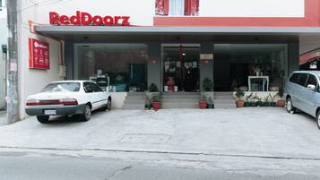 Un edificio RedDoorz con un acceso cubierto, dos coches aparcados y plantas en macetas al frente.