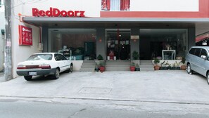 A RedDoorz building with a covered entrance, two parked cars, and potted plants in front. - Reddoorz Near Fernwoods Garden Quezon City (Quezon City)