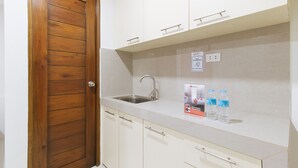 A kitchen with a wooden door, white cabinets, a stainless steel sink, and a RedDoorz discount sign. - Reddoorz Near Fernwoods Garden Quezon City (Quezon City)