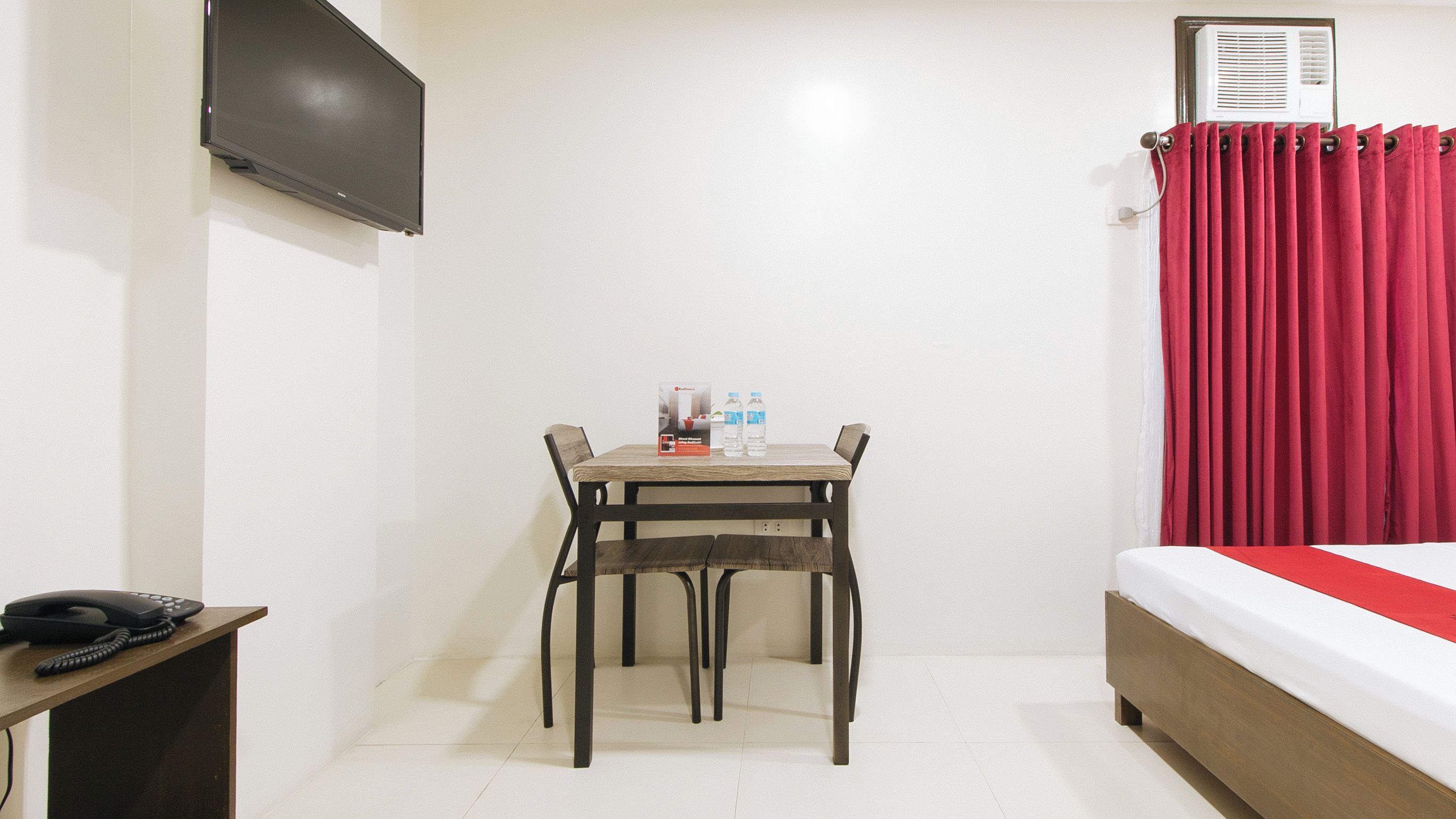 Une chambre d’hôtel avec un lit, un téléviseur fixé au mur, une table avec deux bouteilles d’eau et un téléphone sur une table d’appoint.