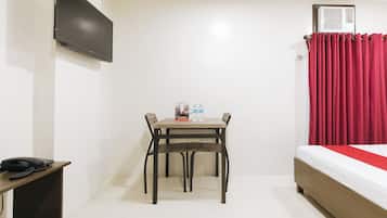 Une chambre d’hôtel avec un lit, un téléviseur fixé au mur, une table avec deux bouteilles d’eau et un téléphone sur une table d’appoint.