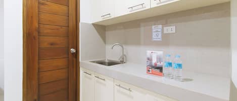 A kitchen with a wooden door, a stainless steel sink, and a countertop with a RedDoorz discount sign and bottled water.