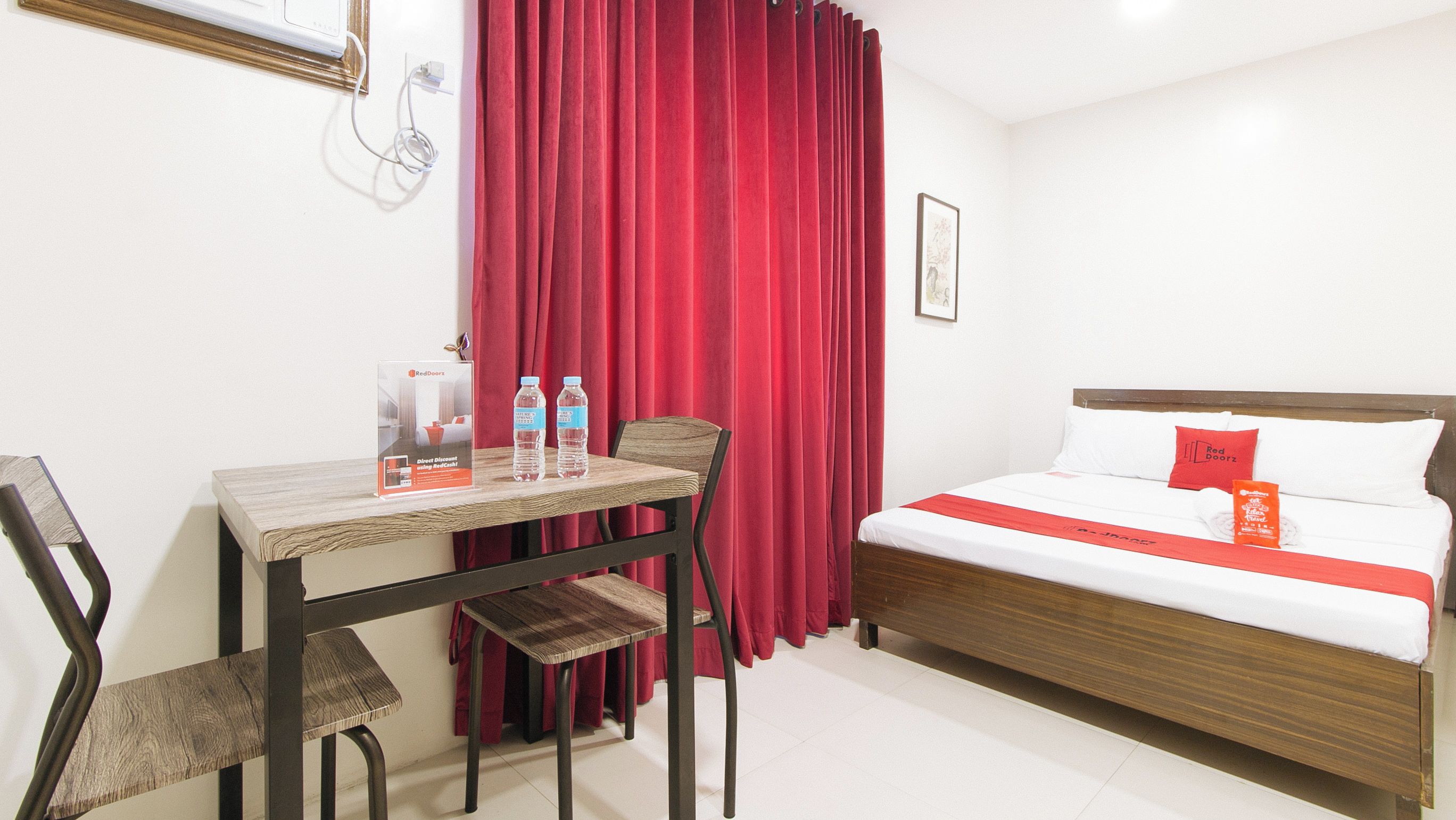Une chambre d’hôtel avec un lit, un bureau et des chaises. Il y a deux bouteilles d’eau sur le bureau.