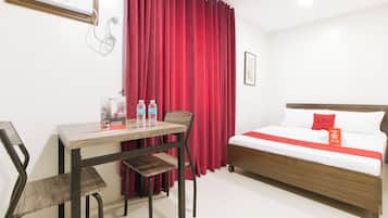 Une chambre d’hôtel avec un lit, un bureau et des chaises. Il y a deux bouteilles d’eau sur le bureau.