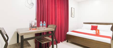 A hotel room with a bed, a desk, and chairs. There are two water bottles on the desk.