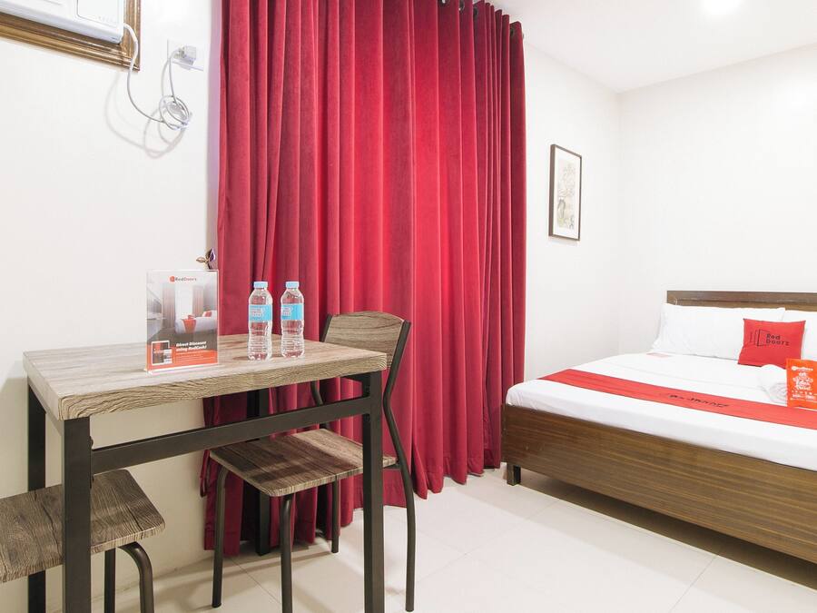 A hotel room with a bed, a desk, and chairs. There are two water bottles on the desk.