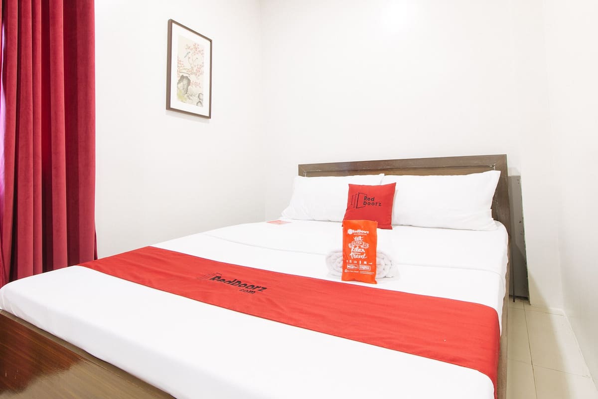 A hotel room with a neatly made bed, red curtains, and a framed picture on the wall.