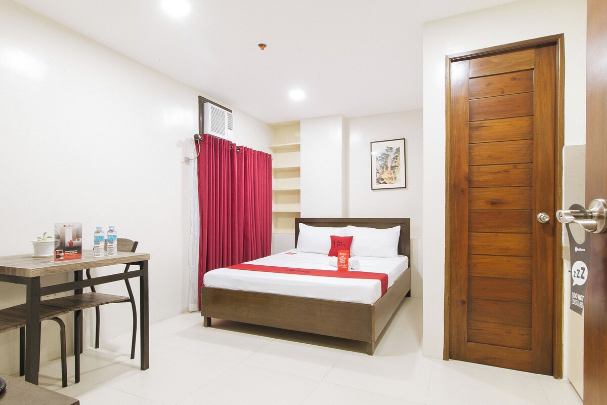 Habitación de hotel con cama, escritorio, silla, teléfono y puerta.