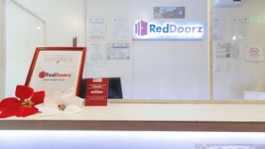 Un mostrador de recepción con un letrero de RedDoorz, certificados enmarcados y un cartel de prohibido fumar.