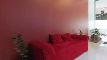 A red sofa against a red wall with a potted plant beside it.