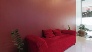 A red sofa against a red wall with a potted plant beside it. - Reddoorz Near Fernwoods Garden Quezon City (Quezon City)