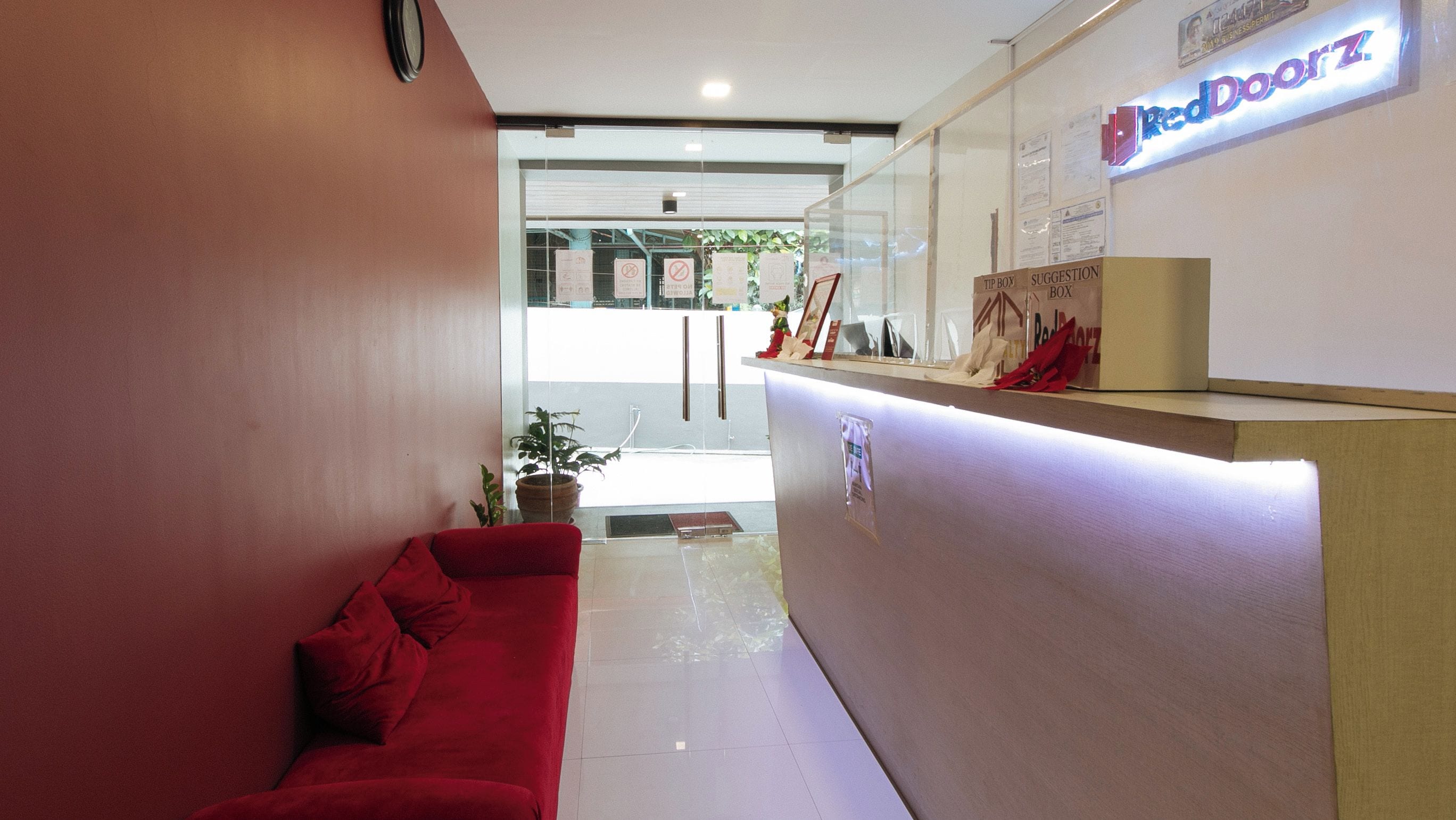Zona de recepción con un sofá rojo, un separador de vidrio y un mostrador de recepción con un cartel que dice 'Red Door Z'.