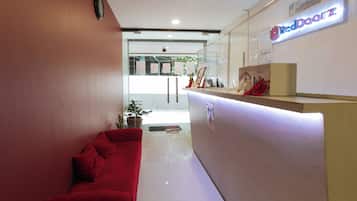 Uma área de recepção com um sofá vermelho, divisória de vidro e um balcão de atendimento com a placa 'Red Door Z'.