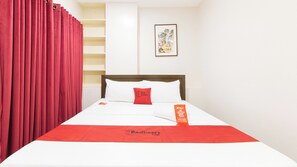 Habitación de hotel con cama, cortina roja, un cuadro en la pared y almohada roja.