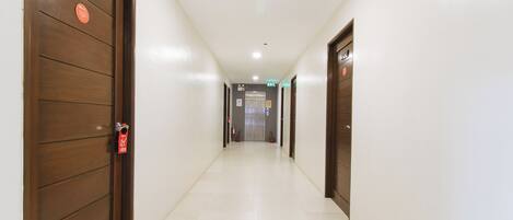 A hallway with wooden doors, a white tiled floor, and an exit sign.