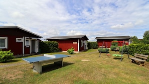 A red building with a door, a ping pong table, and a swing set.