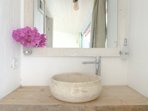 Ein Badezimmer mit einem runden, beige gefärbten Keramikwaschbecken, einer Holzarbeitsplatte, einer weißen Wand und einem Spiegel über dem Waschbecken.