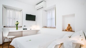 A hotel room with a bed, a desk with a computer, a chair, a TV, and a statue.