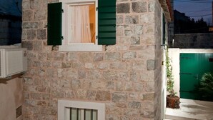 A stone house with a small window and shutters, a door, and a staircase leading to a green gate.