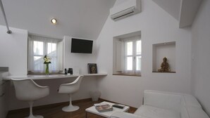 A modern, minimalist living room with a white sofa, two white chairs, a small coffee table, and a TV mounted on the wall.