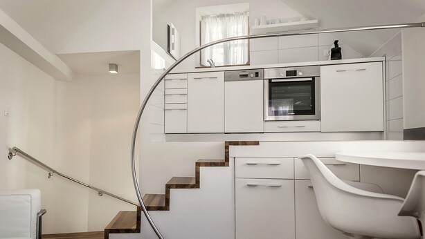 A modern kitchen with white cabinetry, a built-in oven, and a dining area with a white table and chair.