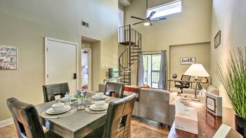 Un coin repas avec une table en bois dressée pour quatre personnes, entourée de chaises en cuir. Un escalier en colimaçon est visible au fond, menant à un niveau supérieur.