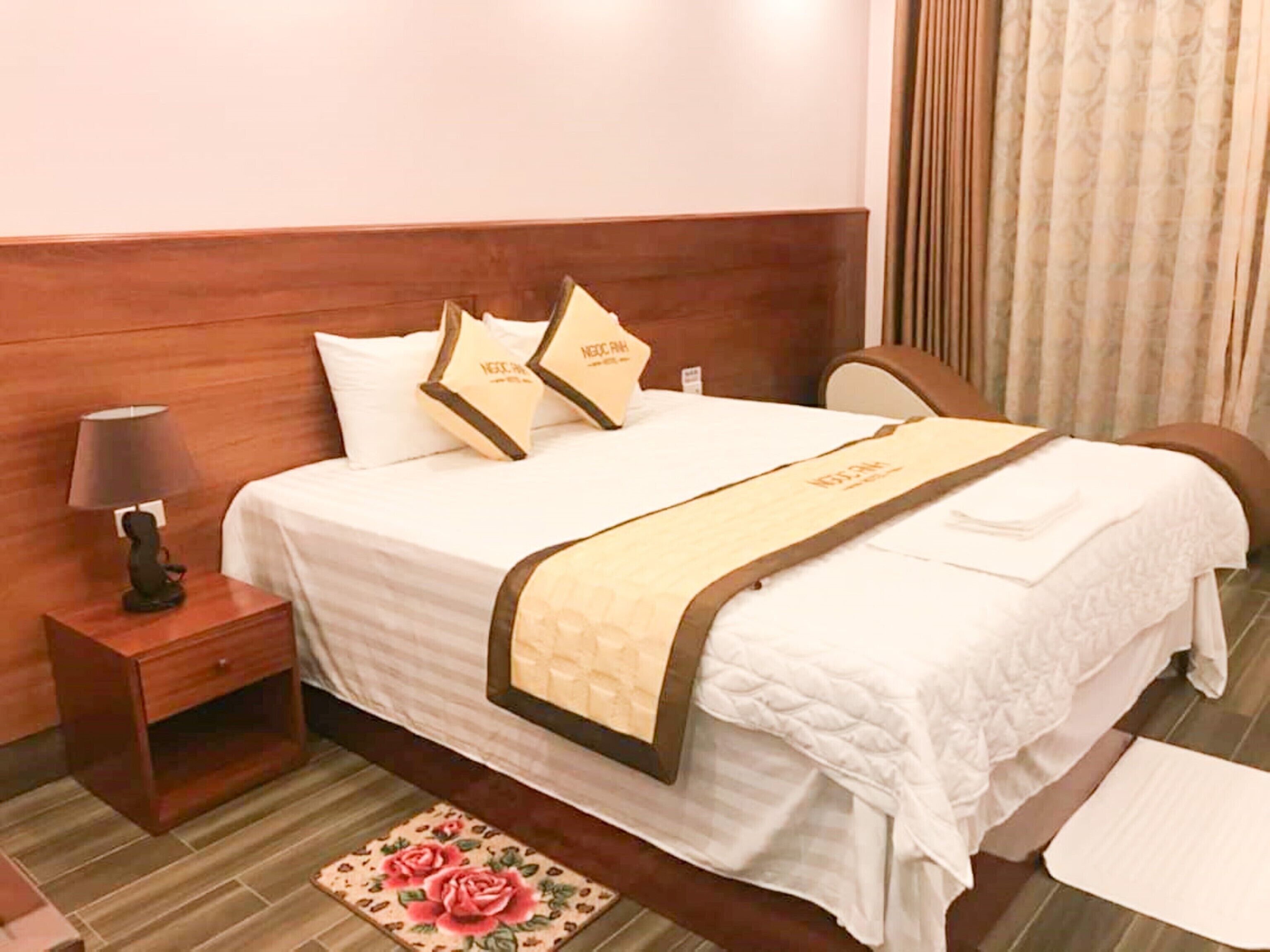 A neatly made bed with a wooden headboard, a bedside table with a lamp, and a floral-patterned rug.