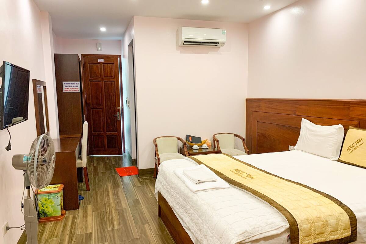 Habitació d'hotel amb llit, taula de nit, cadira i televisió penjada a la paret.