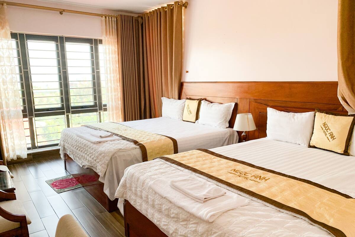 Habitació d'hotel amb dos llits, un panell de capçalera de fusta, una finestra amb cortines i un paviment de fusta.